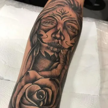 Tatuagem realismo preto e cinza de catrina com rosa no antebraço