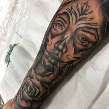 Tatuagem realismo preto e cinza de catrina com rosas no antebraço