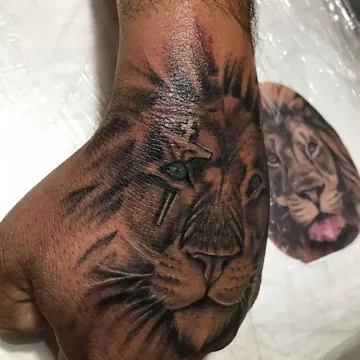 Tatuagem realismo preto e cinza de leão com cruz na mão