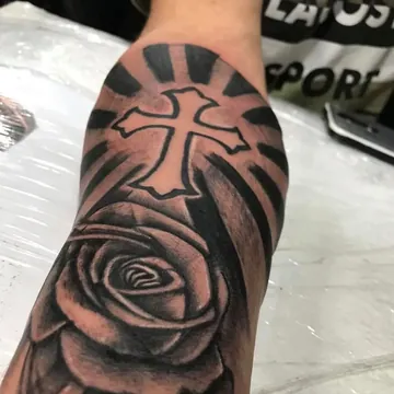 Tatuagem realismo preto e cinza de cruz com rosa no braço
