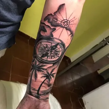 Tatuagem preto e cinza de bússola, mapa e coqueiros no antebraço